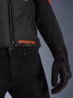 Giacca in pelle Alpinestars GP Plus R V4 Airflow, primo piano di vita e manica, pelle nera traforata con scritte in rosso fluo 'Advanced Racewear Engineering', abbinata a pantaloni da moto neri e guanto da moto SPX 7
