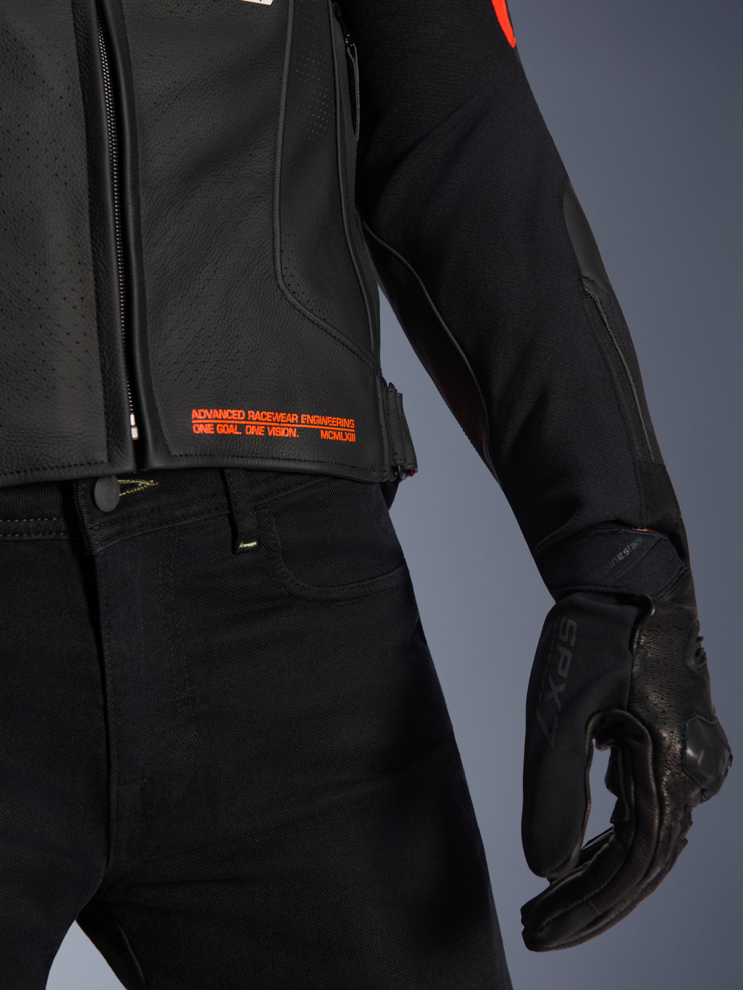 Giacca in pelle Alpinestars GP Plus R V4 Airflow, primo piano di vita e manica, pelle nera traforata con scritte in rosso fluo 'Advanced Racewear Engineering', abbinata a pantaloni da moto neri e guanto da moto SPX 7