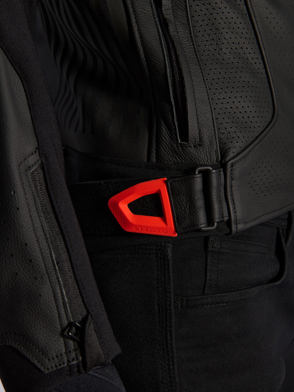 Giacca in pelle Alpinestars GP Plus R V4 Airflow in primo piano, pelle nera traforata con cinghia di regolazione in vita a strappo rosso fluo vivace, tasca laterale con zip e pannelli ergonomici testurizzati.