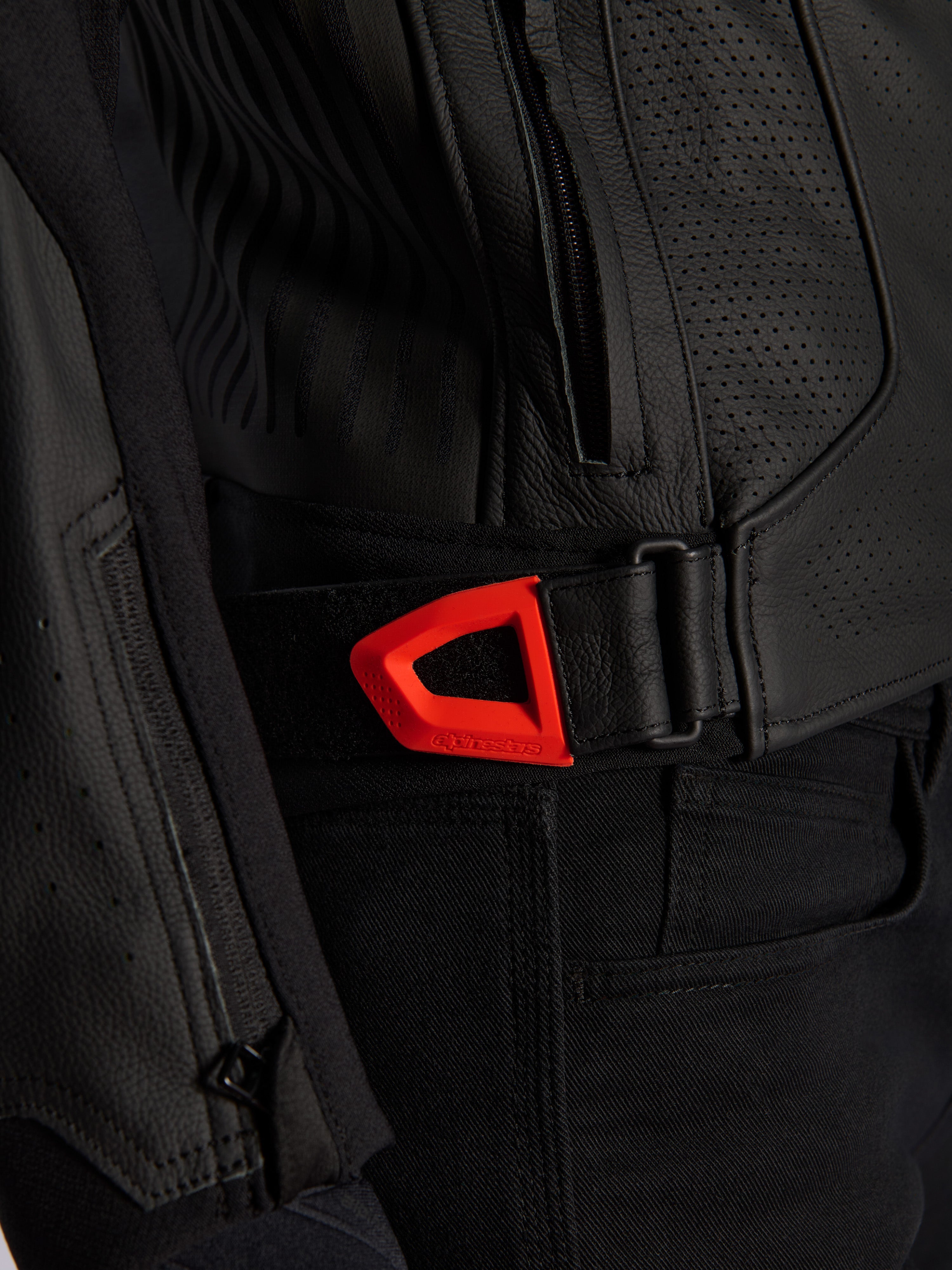 Giacca in pelle Alpinestars GP Plus R V4 Airflow in primo piano, pelle nera traforata con cinghia di regolazione in vita a strappo rosso fluo vivace, tasca laterale con zip e pannelli ergonomici testurizzati.