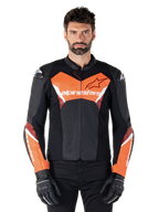 Giacca in pelle Alpinestars Faster V3, giacca da moto sportiva, nero e rosso fluo, indossata da un modello uomo con guanti e pantaloni da moto neri, con logo Alpinestars su petto e avambracci, realizzata in pelle premium per la guida su strada.