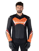 Giacca in pelle Alpinestars Faster V3, giacca da moto sportiva, nero e rosso fluo, indossata da un modello uomo con guanti e pantaloni da moto neri, con logo Alpinestars su petto e avambracci, realizzata in pelle premium per la guida su strada.