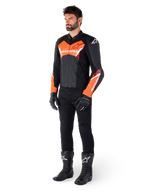 Motociclista che indossa la giacca in pelle Alpinestars Faster V3 in nero e rosso fluo, abbinata a pantaloni da moto, guanti e stivali neri. La giacca presenta una silhouette di derivazione racing con audaci accenti rosso fluorescente su petto e maniche, marchio Alpinestars bianco e una struttura in pelle premium.