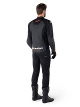 Giacca in pelle Alpinestars Faster V3, giacca da moto sportiva, nero e rosso fluo, vista posteriore indossata con pantaloni neri e stivali neri, con scritta 'alpinestars RACING AHEAD' sulla parte inferiore della schiena e un piccolo logo a stella rosso, struttura in pelle dal taglio sportivo