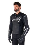 Giacca in pelle Alpinestars Faster V3, giacca da moto sportiva, nero e bianco, prominente logo Alpinestars bianco e scritta 'Racing Ahead' sul petto, loghi a stella sulle spalle, costruzione in pelle premium con pannelli elasticizzati, indossata da un modello con pantaloni e guanti neri