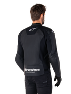 Giacca in pelle Alpinestars Faster V3, nero e bianco, vista posteriore su un pilota, con logo a stella bianco sulla parte superiore della schiena e grande marchio Alpinestars con "Racing Ahead" sulla parte inferiore del retro, retro allungato per una maggiore copertura durante la guida, costruzione in pelle sportiva premium