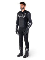 Modello che indossa la giacca in pelle Alpinestars Faster V3, giacca da moto sportiva, nero e bianco, abbinata a pantaloni, guanti e stivali da moto neri, con branding e loghi bianchi, silhouette sportiva per corse su strada