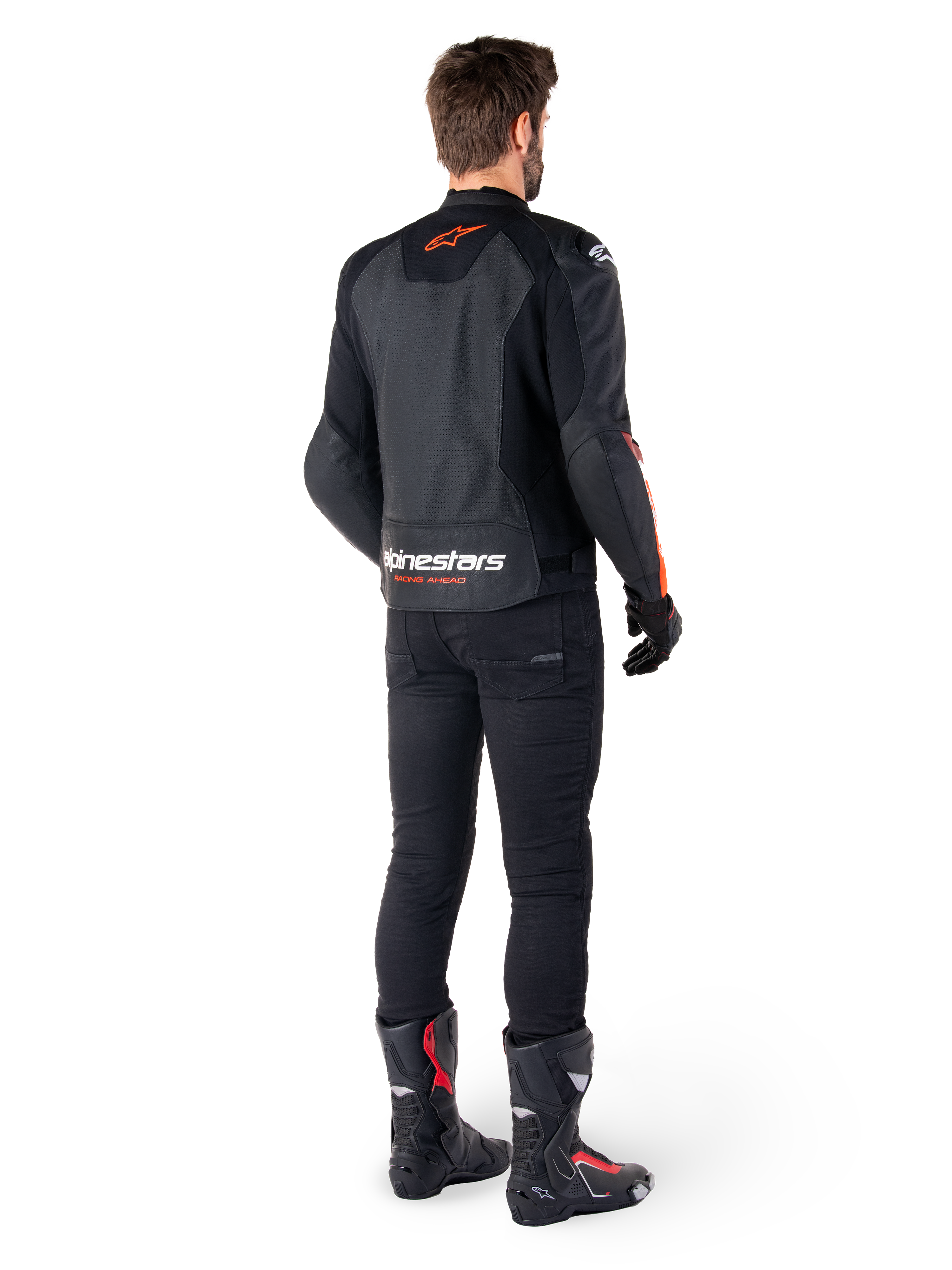 Giacca in pelle Alpinestars Faster V3 Airflow, nero e rosso fluo, vista da dietro su un pilota, con pannelli in pelle traforata e loghi evidenti, indossata con pantaloni neri e stivali da moto, abbigliamento da guida sportiva.