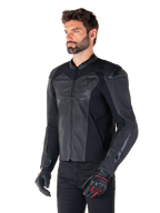 Modello che indossa la giacca in pelle Alpinestars Faster V3 Airflow in Black Black, giacca da moto sportiva con pelle traforata e pannelli elasticizzati, abbinata a pantaloni neri e guanti neri con accenti rossi, stile raffinato di derivazione racing