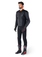 Uomo che indossa la giacca in pelle Alpinestars Faster V3 Airflow in Nero Nero, abbinata a pantaloni neri, guanti da moto neri e rossi e stivali da corsa neri con dettagli rossi e bianchi, equipaggiamento da guida sportiva completo