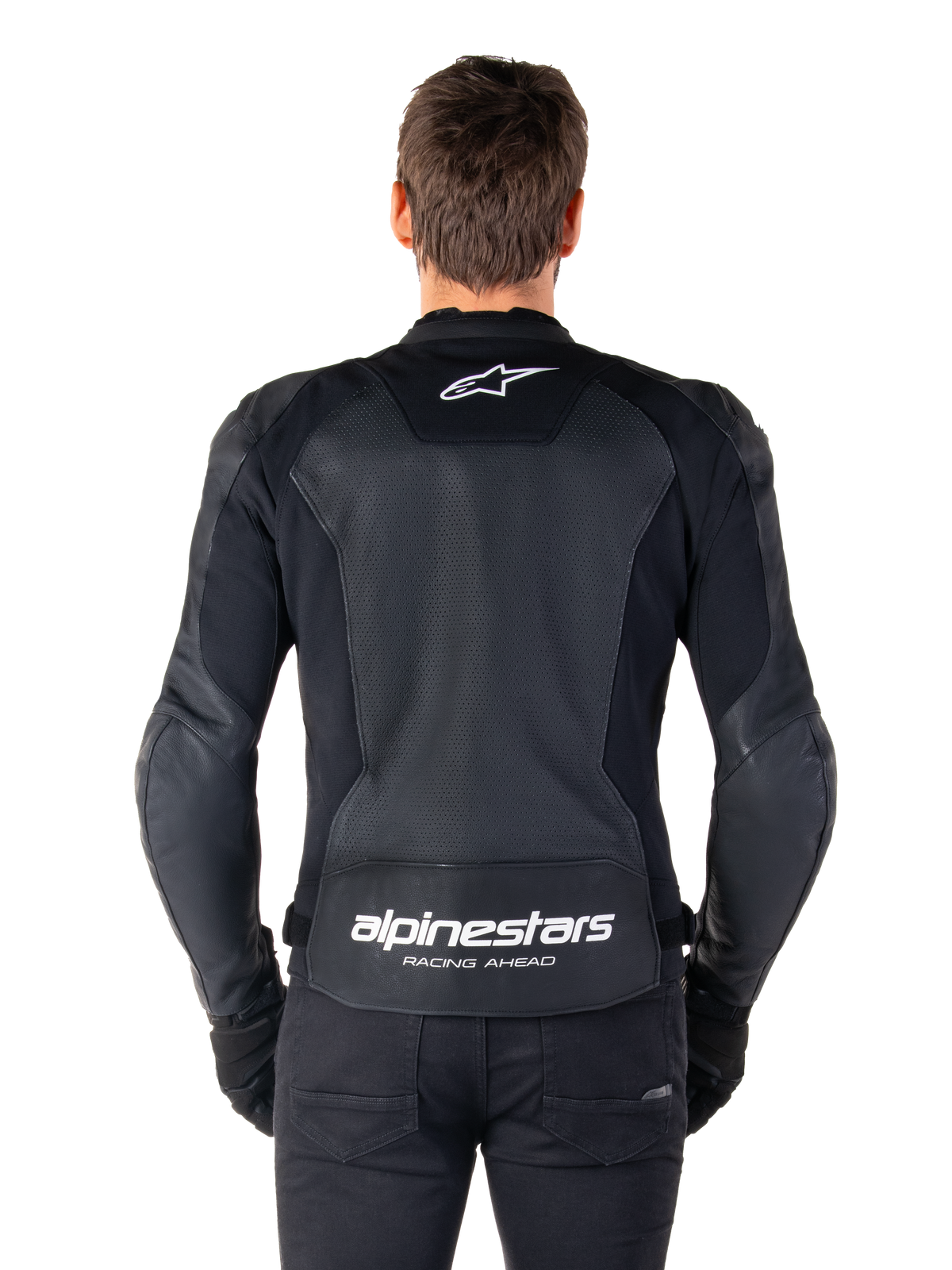Giacca in pelle Alpinestars Faster V3 Airflow, nero e bianco, vista posteriore di un pilota che mostra il pannello posteriore in pelle traforata per la ventilazione, logo Alpinestars bianco sulla parte superiore della schiena e marchio 'RACING AHEAD' sulla parte inferiore della schiena, abbigliamento da moto sportivo.