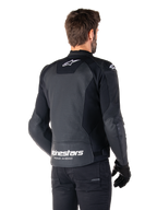 Giacca in pelle Alpinestars Faster V3 Airflow, nero e bianco, vista posteriore su un modello, con schiena in pelle traforata per la ventilazione, loghi Astars bianchi e scritta 'Racing Ahead', design sportivo con pannelli elasticizzati per il motociclismo.