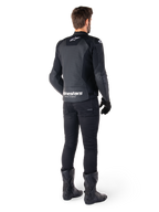 Giacca in pelle Alpinestars Faster V3 Airflow, nera e bianca, vista posteriore che mostra i pannelli in pelle traforata e il marchio Alpinestars sulla parte bassa della schiena, indossata da un motociclista con pantaloni, guanti e stivali neri.