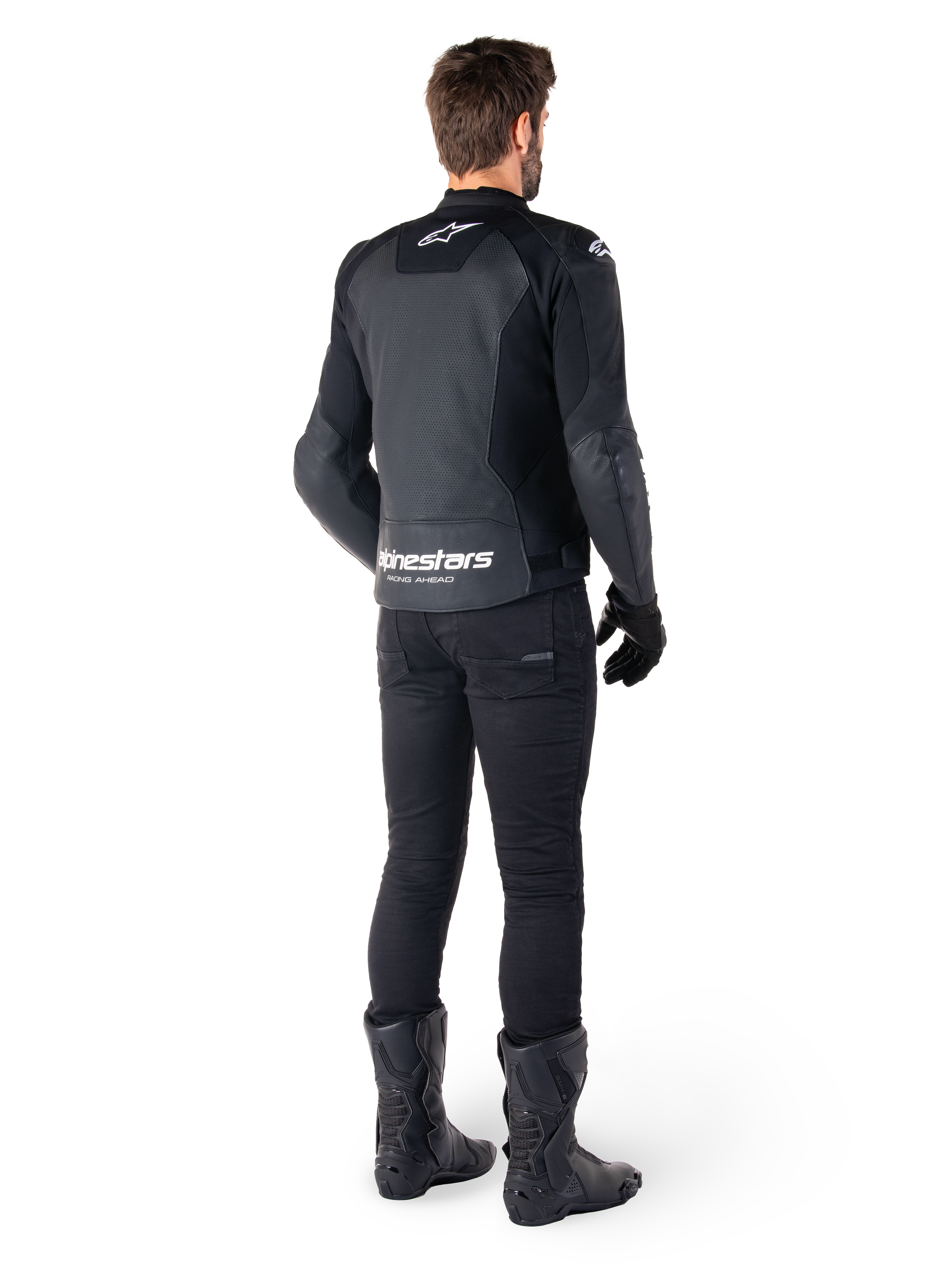 Giacca in pelle Alpinestars Faster V3 Airflow, nera e bianca, vista posteriore che mostra i pannelli in pelle traforata e il marchio Alpinestars sulla parte bassa della schiena, indossata da un motociclista con pantaloni, guanti e stivali neri.