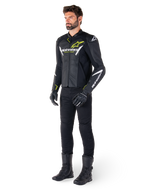 Pilota uomo che indossa la giacca in pelle Alpinestars Faster V3 Airflow in nero, bianco e giallo fluo, abbinata a pantaloni e stivali da moto neri, con pannelli in pelle traforata, dettagli del logo bianchi e accenti giallo neon, abbigliamento tecnico sportivo professionale