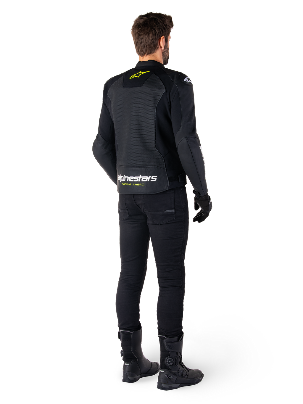 Vista posteriore di un pilota che indossa la giacca in pelle Alpinestars Faster V3 Airflow, nero con dettagli bianchi e giallo fluo, abbinata a pantaloni e stivali neri, con pelle traforata per la ventilazione e il marchio 'RACING AHEAD' sulla parte bassa della schiena.