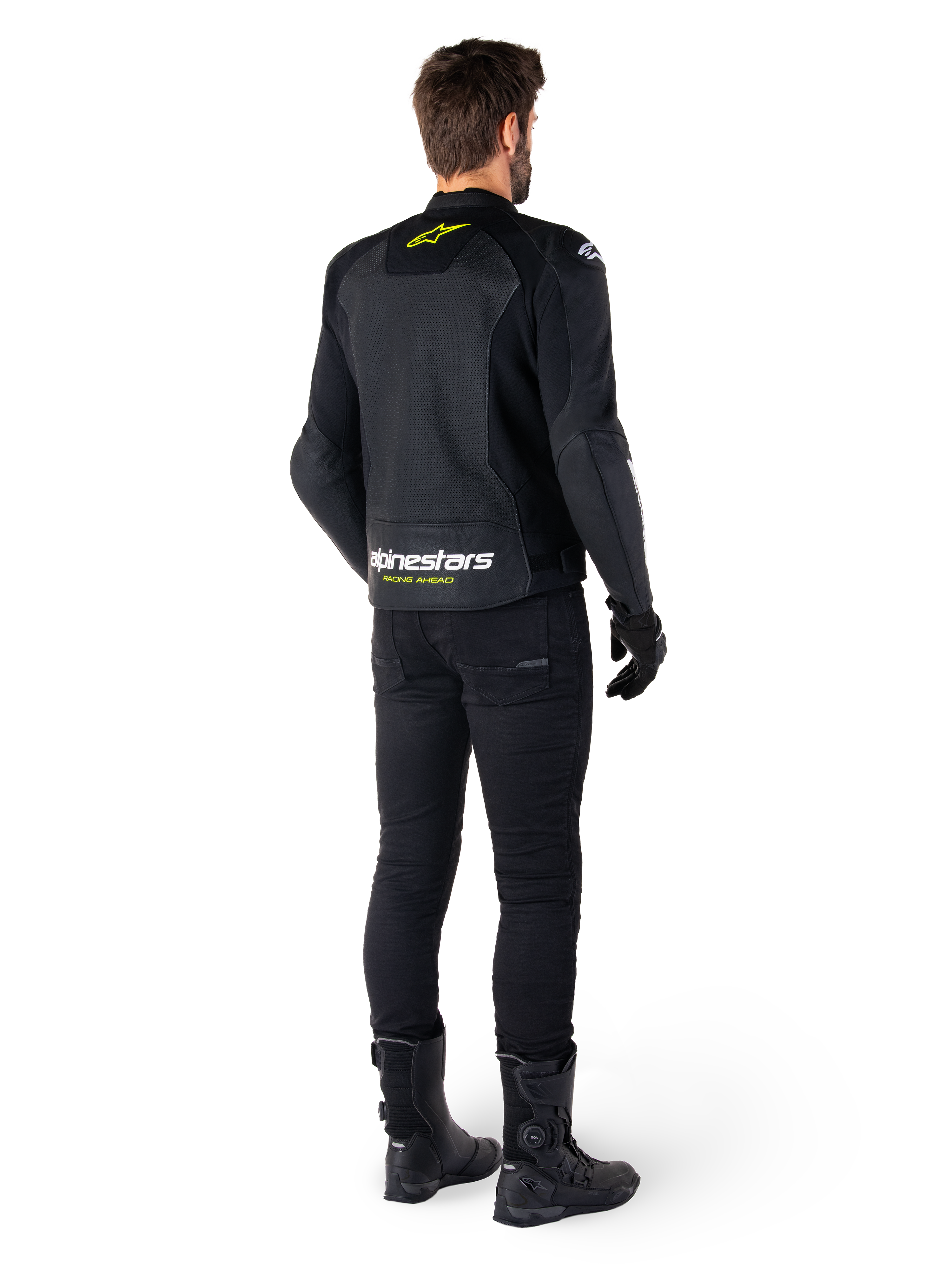 Vista posteriore di un pilota che indossa la giacca in pelle Alpinestars Faster V3 Airflow, nero con dettagli bianchi e giallo fluo, abbinata a pantaloni e stivali neri, con pelle traforata per la ventilazione e il marchio 'RACING AHEAD' sulla parte bassa della schiena.