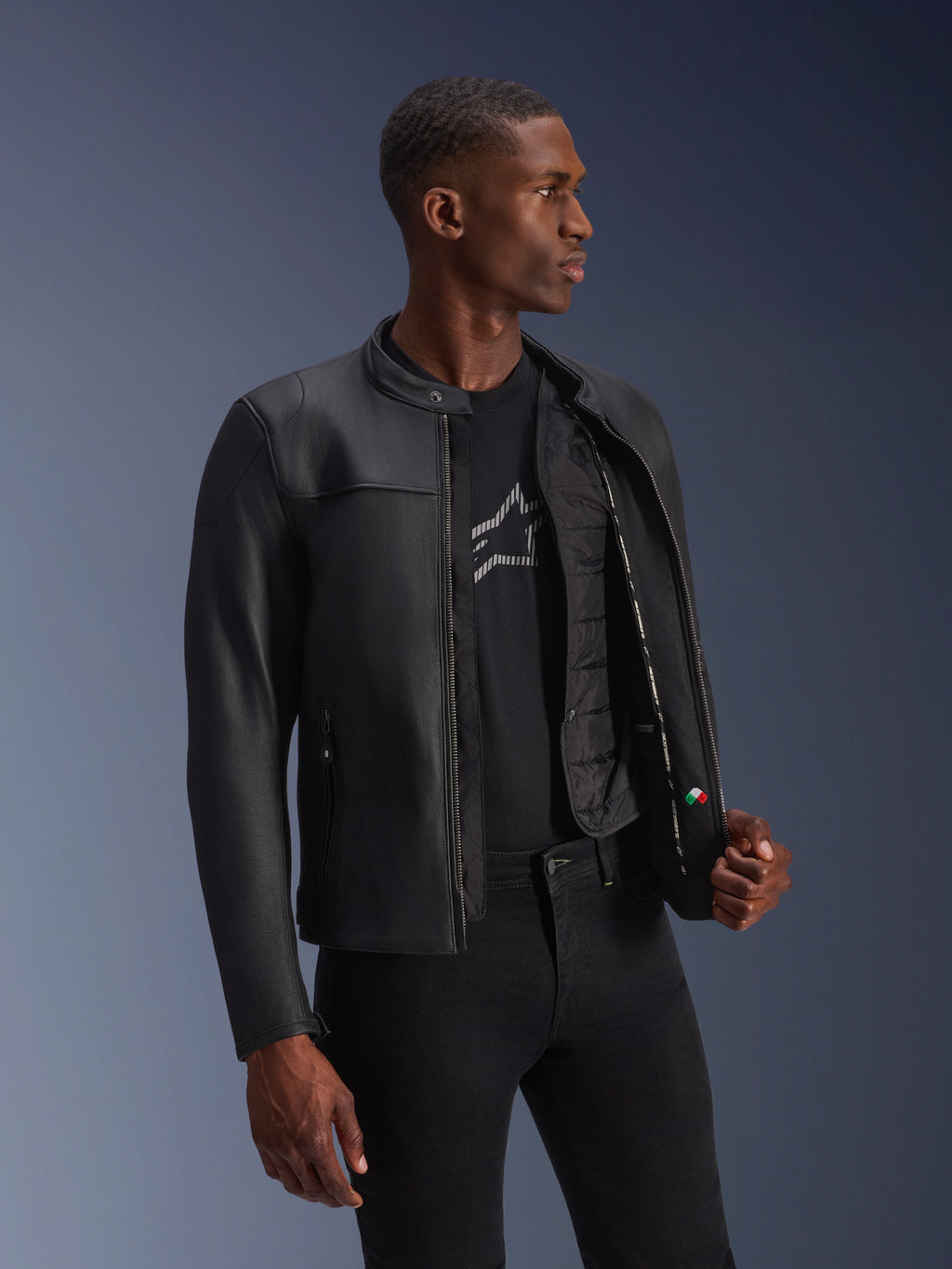 Giacca in pelle Alpinestars Blacktrack, nera, pelle bovina di alta qualità con vestibilità su misura, aperta per mostrare il gilet termico rimovibile e i dettagli interni, indossata da un modello, abbigliamento da moto urbano moderno