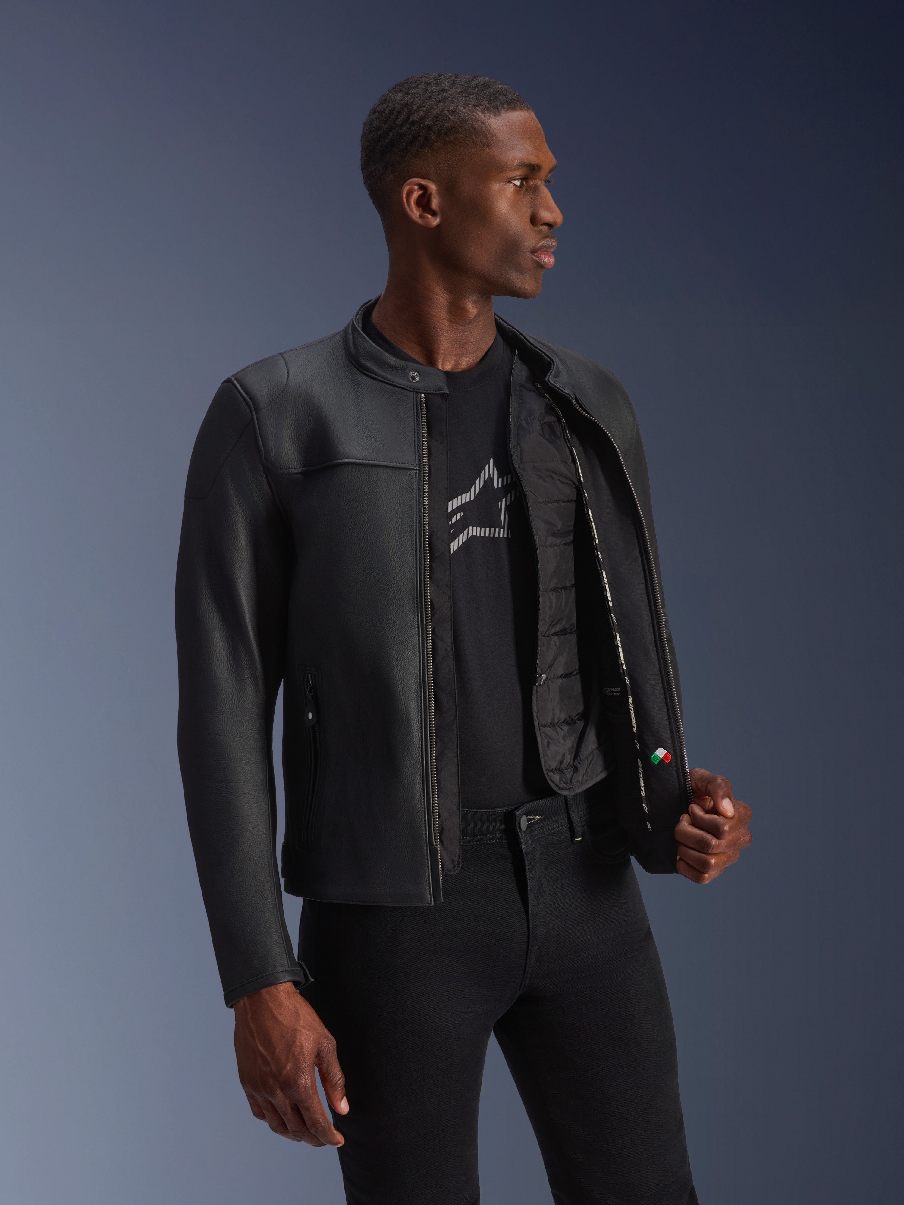 Giacca in pelle Alpinestars Blacktrack, nera, pelle bovina di alta qualità con vestibilità su misura, aperta per mostrare il gilet termico rimovibile e i dettagli interni, indossata da un modello, abbigliamento da moto urbano moderno