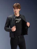 Giacca in pelle Alpinestars Dyno, nero, indossata da un modello sopra una t-shirt nera con logo, giacca da moto in pregiata pelle bovina con design d'ispirazione heritage, sottili strisce sul petto e vestibilità urbana contemporanea