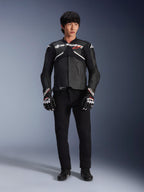 Modello che indossa la giacca in pelle Alpinestars Atem V5 in nero e bianco, con marchio Alpinestars bianco e logo con stella rossa sul petto, abbinata a pantaloni neri e guanti da corsa bianchi e neri, abbigliamento da moto performante ed elegante