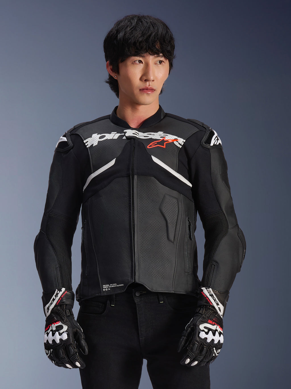Alpinestars Atem V5 Leather Jacket, giacca da moto racing, nera con accenti bianchi e rossi, costruzione in pelle premium con protezioni rinforzate, indossata con guanti da corsa coordinati