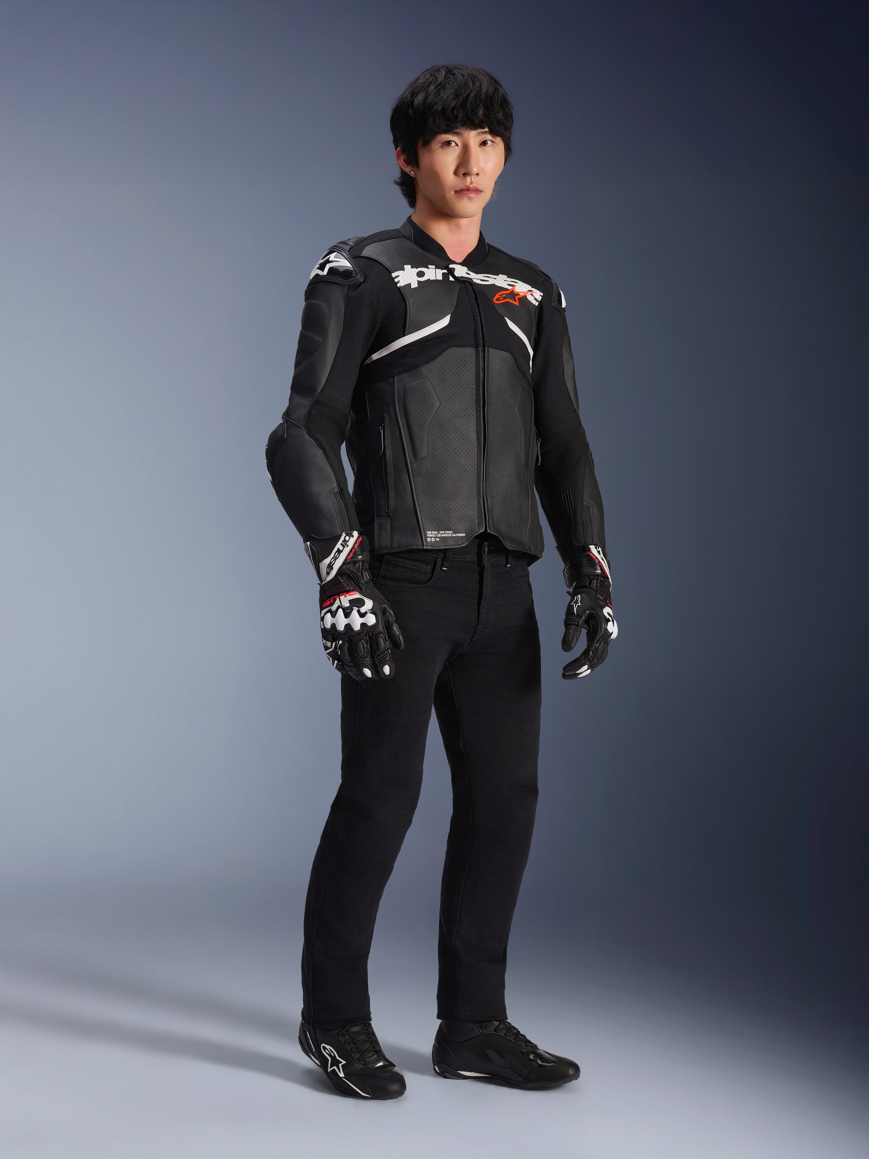 Giacca in pelle Alpinestars Atem V5, giacca da moto racing, nero e bianco, indossata con pantaloni neri e guanti coordinati, con logo Alpinestars bianco sul petto e protezioni sulle spalle