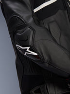 Giacca in pelle Alpinestars Atem V5, nero e bianco, primo piano della protezione per gomiti DFS RR con logo a stella bianco, pelle a fisarmonica e trame traforate per la guida sportiva