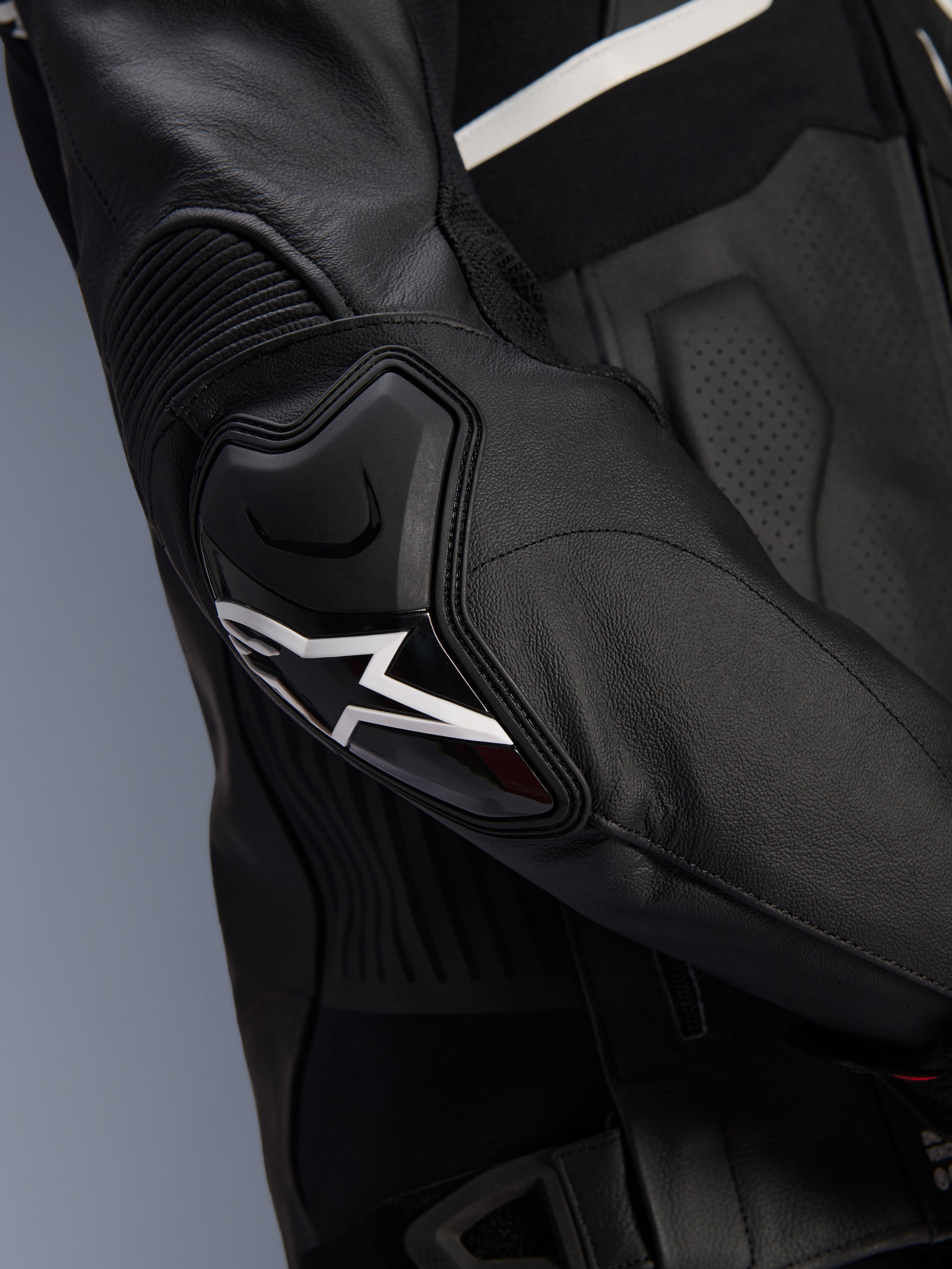 Giacca in pelle Alpinestars Atem V5, nero e bianco, primo piano della protezione per gomiti DFS RR con logo a stella bianco, pelle a fisarmonica e trame traforate per la guida sportiva