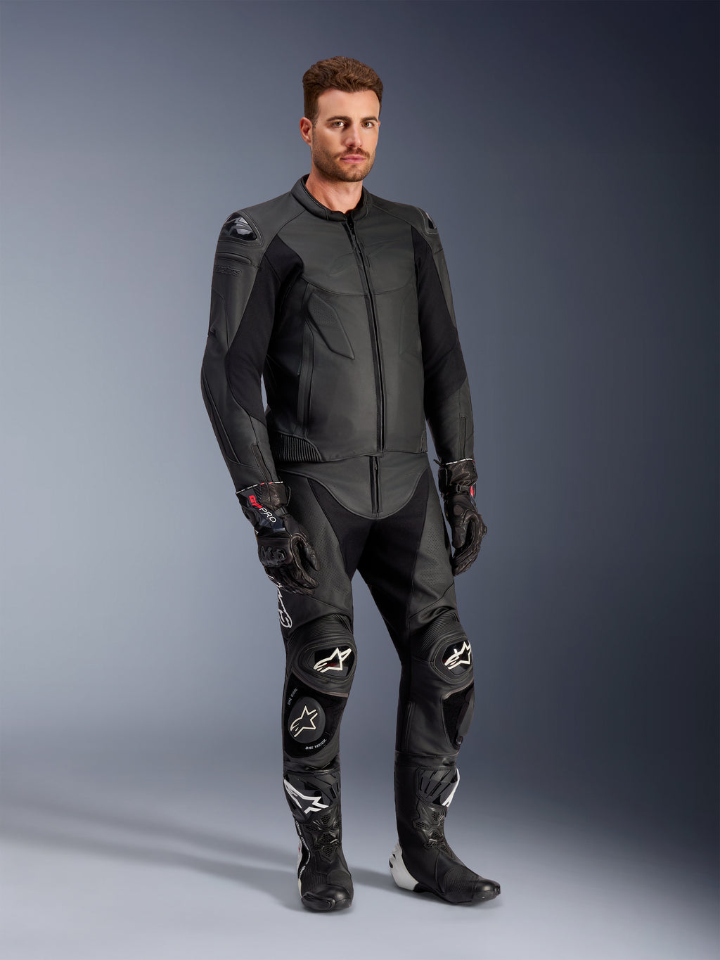 Modello che indossa la giacca in pelle Alpinestars Caliber in nero, abbinata a pantaloni da moto in pelle nera coordinati, guanti racing e stivali, mostrando un outfit completo da strada sportivo.