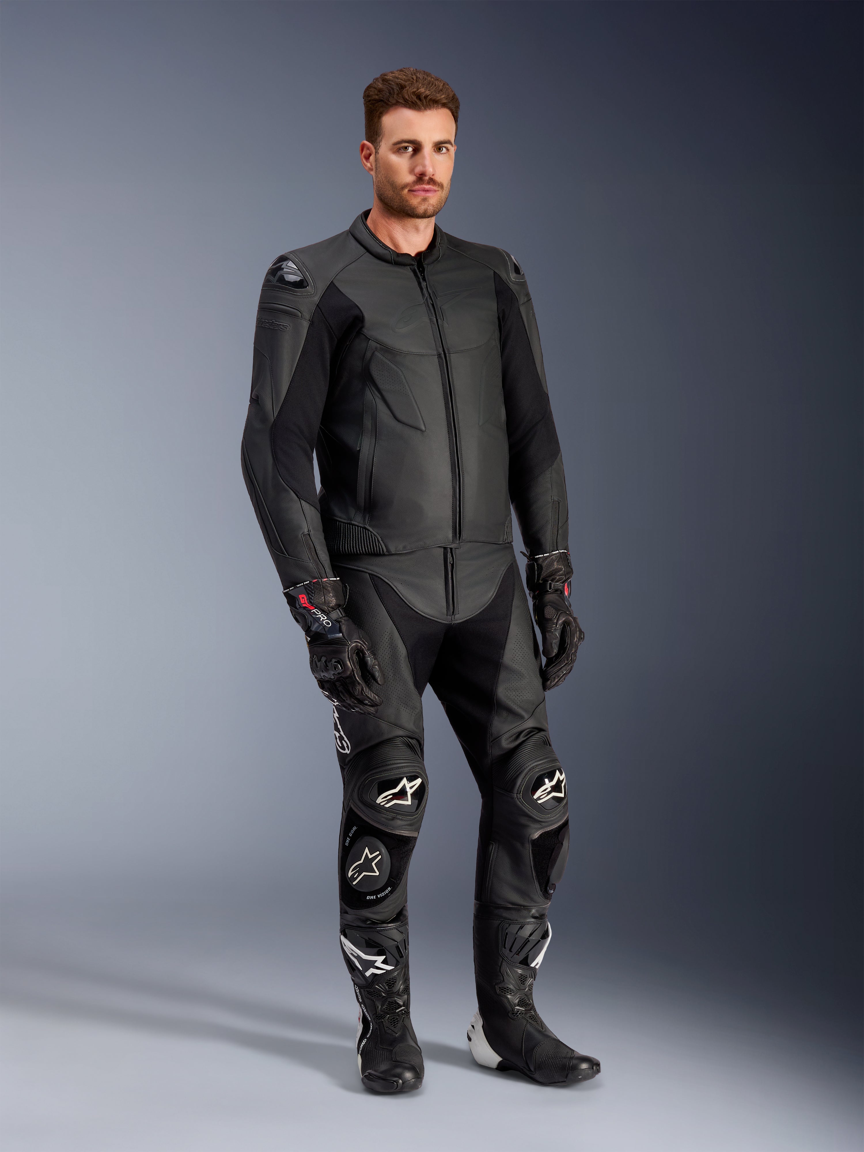 Modello che indossa la giacca in pelle Alpinestars Caliber in nero, abbinata a pantaloni da moto in pelle nera coordinati, guanti racing e stivali, mostrando un outfit completo da strada sportivo.