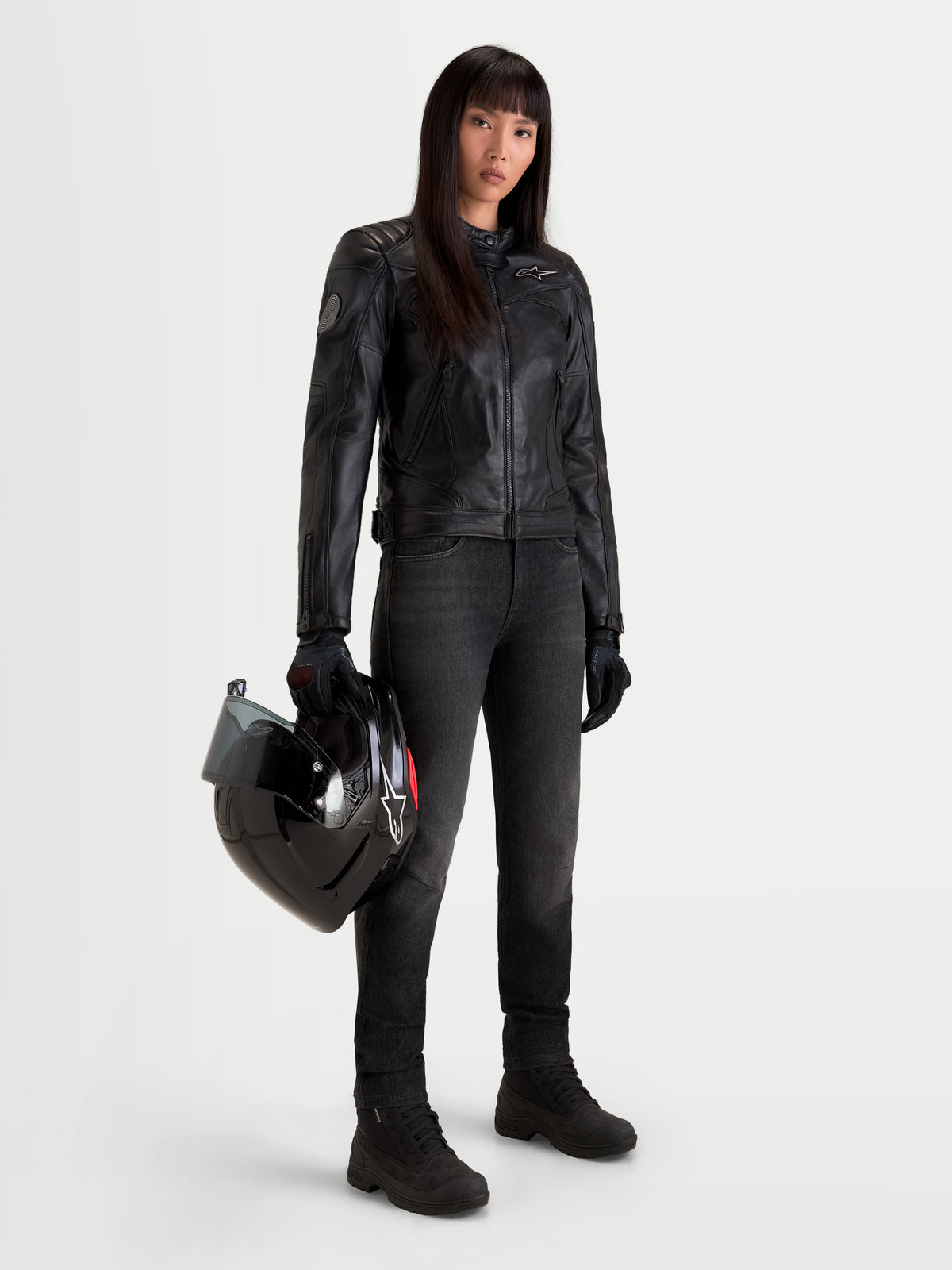 Alpinestars Revea Donna Giacca di pelle, giacca da moto urbana contemporanea da donna in pelle nera, indossata da una modella che tiene un casco in mano, protezione certificata AA