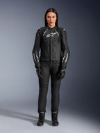 Giacca in pelle Alpinestars Stella Dusk da donna, nero e bianco, indossata da una modella con pantaloni e stivali neri coordinati, vista frontale, con loghi Alpinestars bianchi sul petto e sulle maniche, equipaggiamento protettivo in pregiata pelle bovina per donna