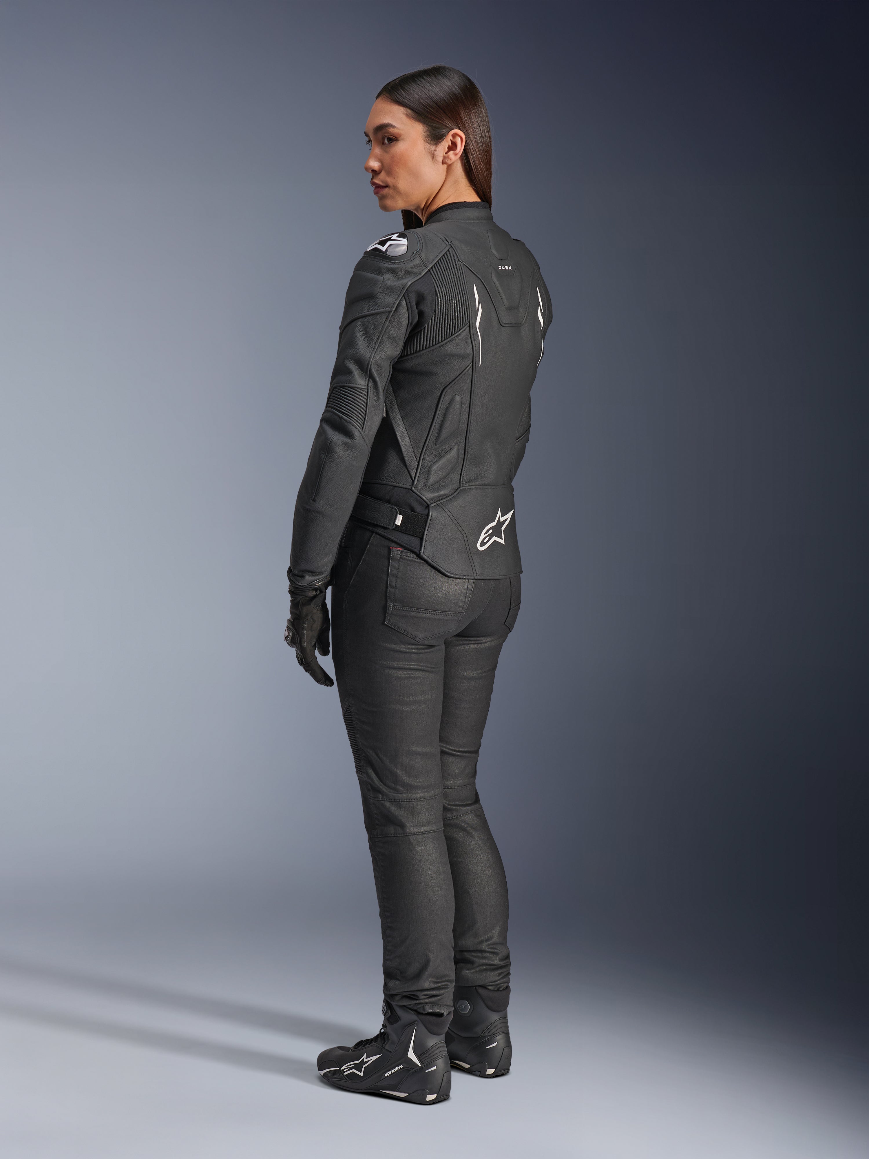 Alpinestars Stella Dusk Leather Jacket, giacca da moto donna, nero e bianco, vista posteriore con logo Alpinestars bianco sulla parte inferiore della schiena e sulle spalle, indossata con pantaloni e stivali da moto neri, vestibilità ergonomica sportiva per la guida su strada