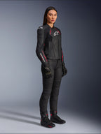Alpinestars Stella Dusk Leather Jacket da donna, nero, rosa Diva e bianco, indossata da una modella con pantaloni e stivali da moto neri, struttura in pelle con dettagli rosa e loghi bianchi