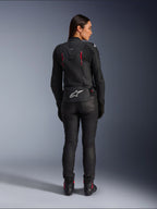 Giacca in pelle Alpinestars Stella Dusk, vista posteriore, pelle nera con accenti Diva Pink e bianchi, presenta il logo Alpinestars bianco sulla parte bassa della schiena e dettagli delle prese d'aria rosa, indossata con pantaloni da moto e stivali neri, abbigliamento sportivo da moto premium per donna