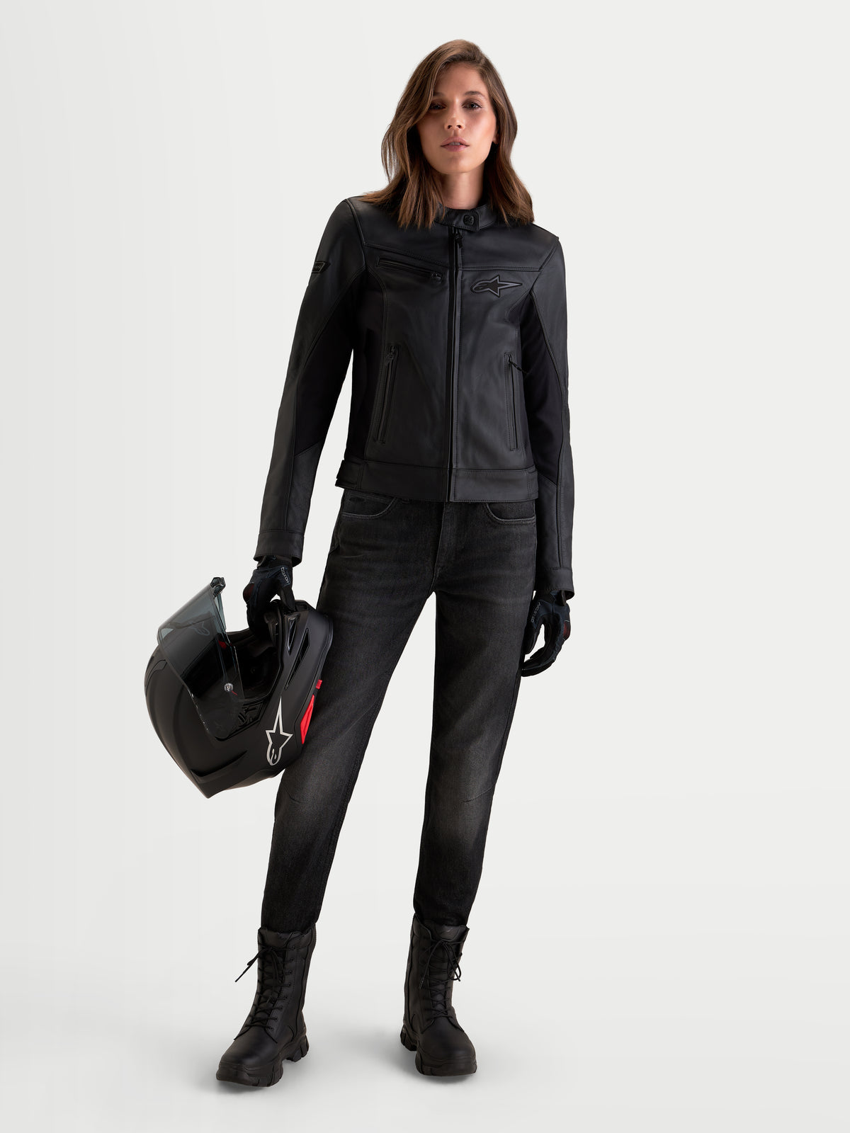 Alpinestars Stella Maver X Giacca di pelle, giacca da moto da donna in pelle nera, vista frontale di una modella che indossa la giacca e tiene in mano un casco, con struttura in morbida pelle bovina e stile urban contemporaneo