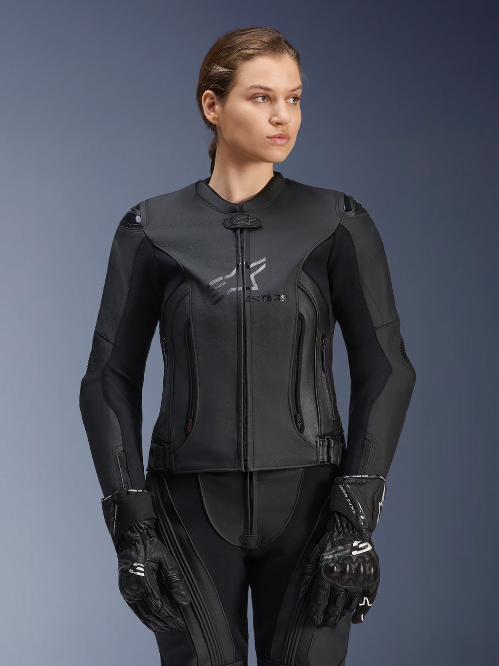 Giacca in pelle Alpinestars Stella GP Plus V4, nera, giacca da moto racing da donna, struttura in pelle premium con imbottitura protettiva, design elegante con logo discreto, indossata da una modella con equipaggiamento nero coordinato