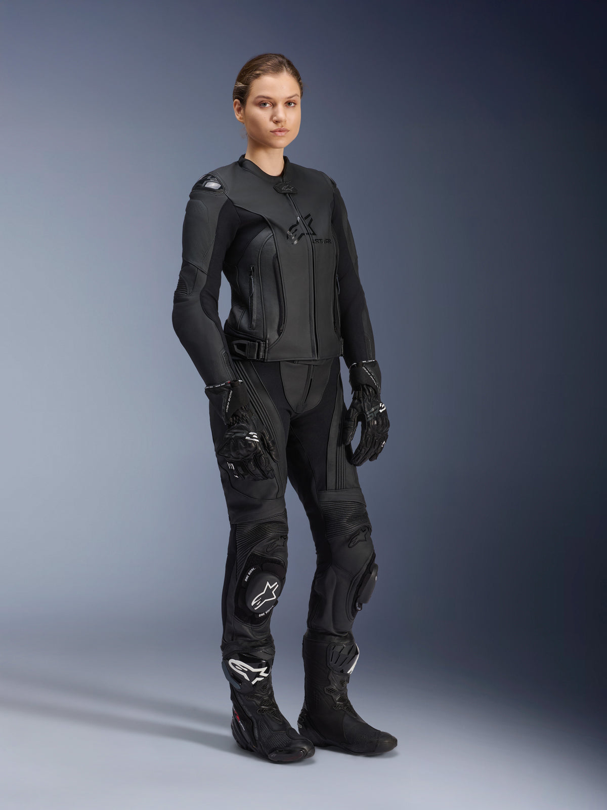 Motociclista con giacca in pelle Alpinestars Stella GP Plus V4 da donna in Black Black, abbinata a pantaloni, guanti e stivali coordinati per creare un completo racing in pelle con design ad alte prestazioni e protezioni integrate.