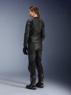 Giacca in pelle Stella GP Plus V4 da donna, nero, vista posteriore completa, abbinata a pantaloni da moto in pelle neri, guanti racing e stivali, con logo Alpinestars goffrato sulla parte bassa della schiena e silhouette aerodinamica per la guida sportiva