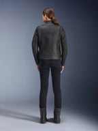 Vista posteriore di una donna che indossa la giacca in pelle Alpinestars Stella Dyno, nero con accenti Haute Red, abbinata a pantaloni neri slim-fit e stivali neri, design moderno heritage di giacca da moto in pelle.