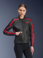 Giacca in pelle Alpinestars Stella Dyno, giacca da moto da donna, nero e rosso, indossata da una modella con jeans neri, con strisce racing rosse su spalle e maniche e branding evidente, realizzata in pelle premium, design d'ispirazione heritage per la guida urbana