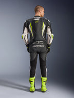 Alpinestars GP Tech V5 One Piece Leather Suit, vista posteriore, nero bianco e giallo fluo, con gobba aerodinamica e logo a stella giallo, marchio Alpinestars bianco su maniche e schiena, stivali da corsa coordinati in giallo neon, abbigliamento professionale da pista per moto