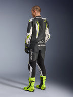 Tuta in pelle intera GP Tech V5 Alpinestars, nero, bianco e giallo fluo, vista posteriore del pilota con tuta da gara e stivali giallo fluo coordinati, caratterizzata da gobba aerodinamica e loghi Alpinestars, abbigliamento professionale da moto