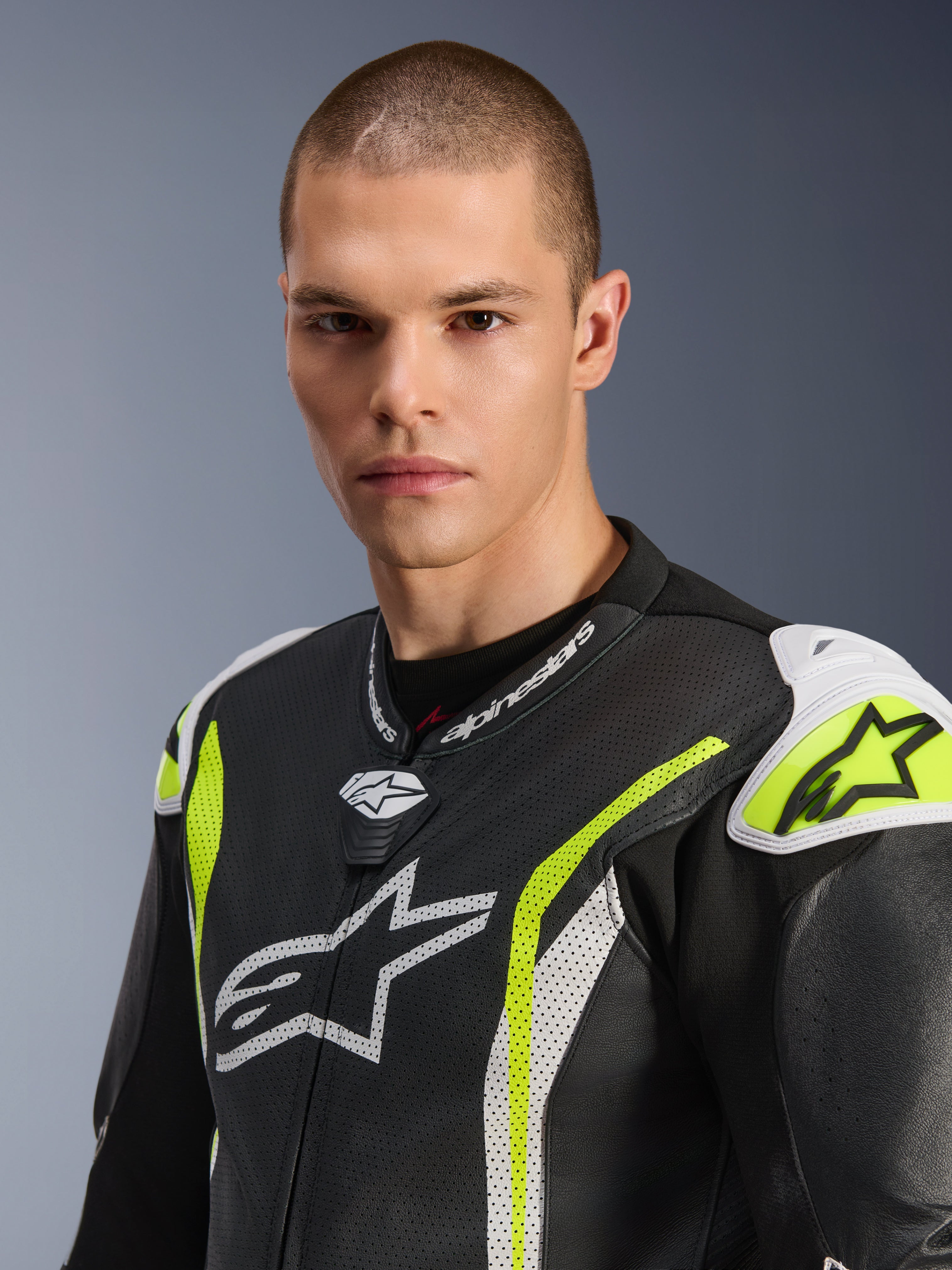 Primo piano di un modello maschile che indossa la tuta in pelle intera Alpinestars GP Tech V5, Nero Bianco Giallo Fluo, con pelle traforata, loghi Alpinestars bianchi sul petto e sulle spalle e accenti giallo vivace, abbigliamento da corsa professionale.