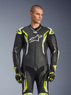 Tuta in pelle intera Alpinestars GP Tech V5, nero, bianco e giallo fluo, equipaggiamento professionale da corsa, pelle traforata con grande logo Astar bianco sul petto, accenti giallo fluorescente e bianchi, indossata con guanti da corsa coordinati