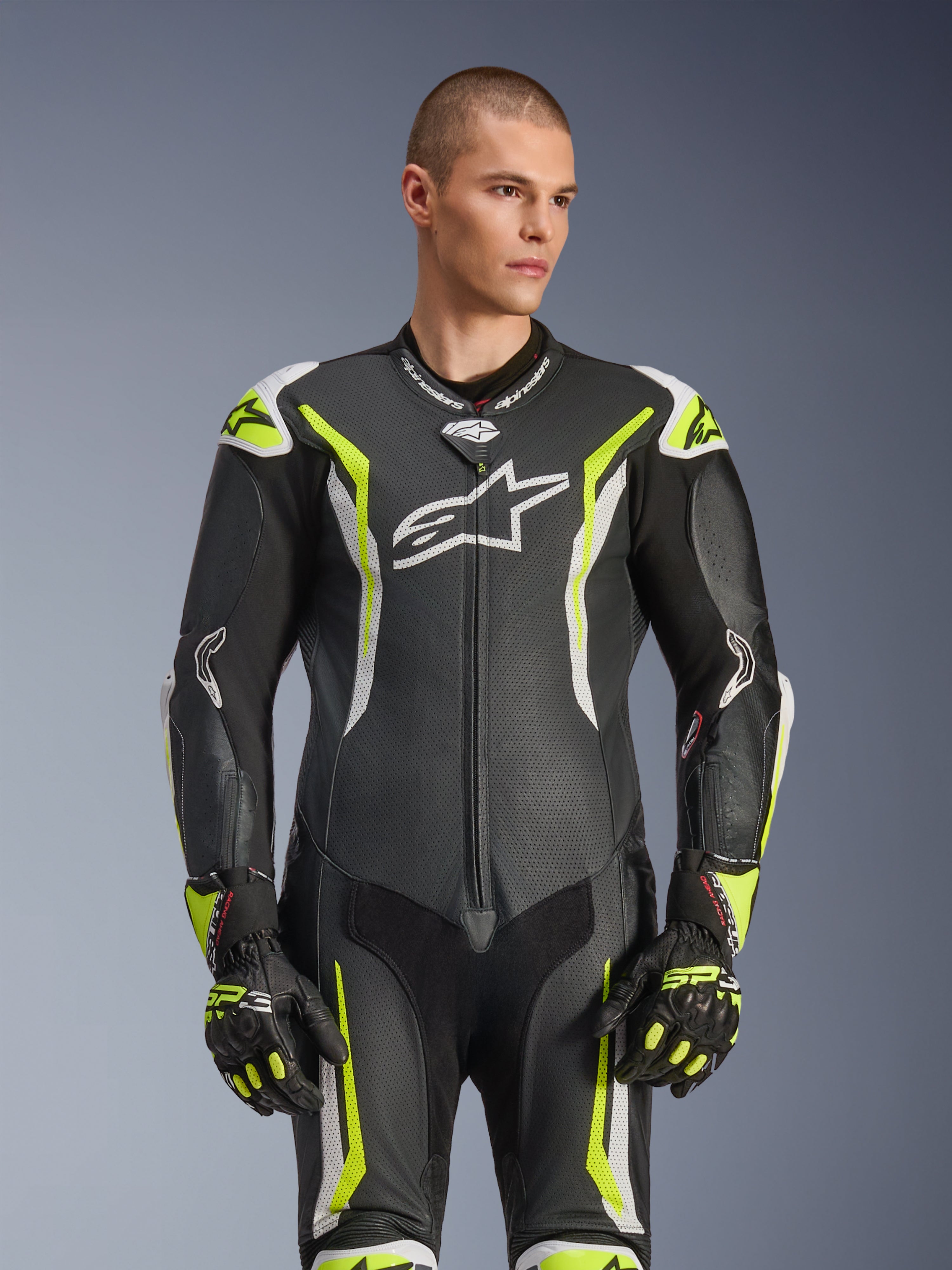 Tuta in pelle intera Alpinestars GP Tech V5, nero, bianco e giallo fluo, equipaggiamento professionale da corsa, pelle traforata con grande logo Astar bianco sul petto, accenti giallo fluorescente e bianchi, indossata con guanti da corsa coordinati