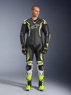 Alpinestars GP Tech V5 One Piece Leather Suit, tuta professionale da moto in pelle monopezzo, nero e giallo neon fluo con dettagli bianchi, indossata da un modello con guanti e stivali da corsa coordinati, design aerodinamico e slider protettivi