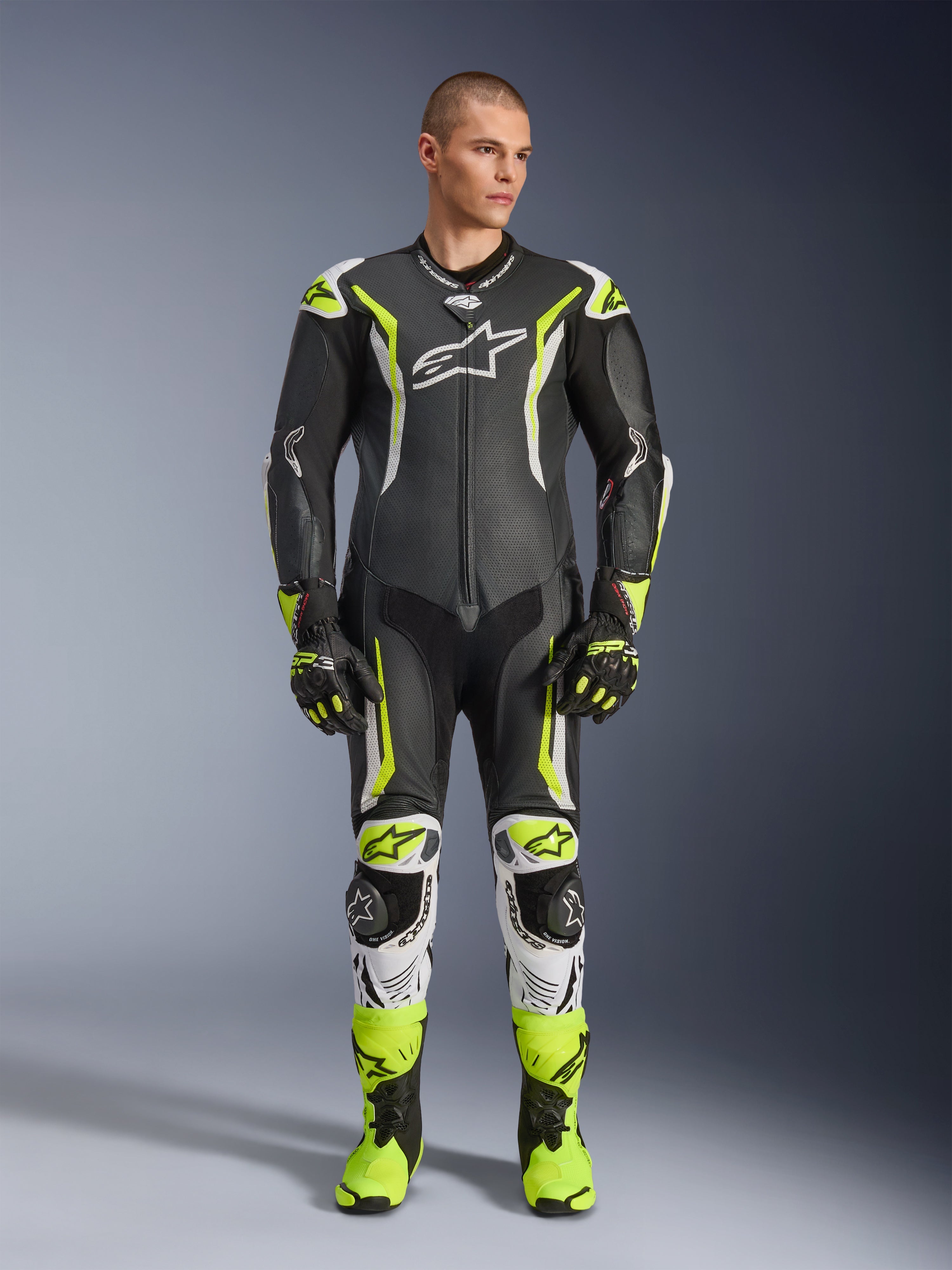 Alpinestars GP Tech V5 One Piece Leather Suit, tuta professionale da moto in pelle monopezzo, nero e giallo neon fluo con dettagli bianchi, indossata da un modello con guanti e stivali da corsa coordinati, design aerodinamico e slider protettivi