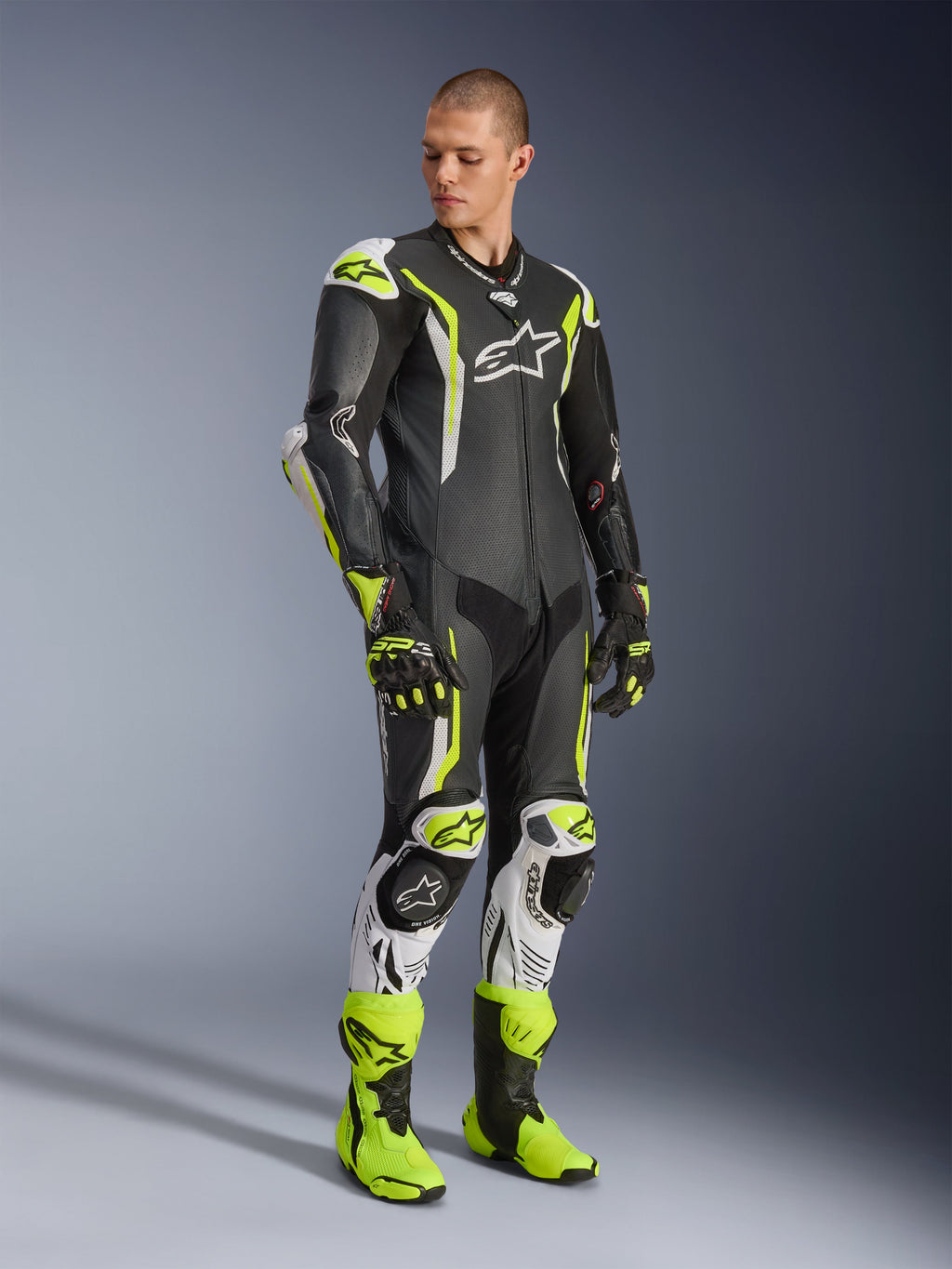 Alpinestars GP Tech V5 One Piece Leather Suit, tuta in pelle intera, nero, bianco e giallo fluo, indossata da un modello con guanti e stivali da corsa coordinati, equipaggiamento professionale per gare motociclistiche con prestazioni aerodinamiche e protezioni.